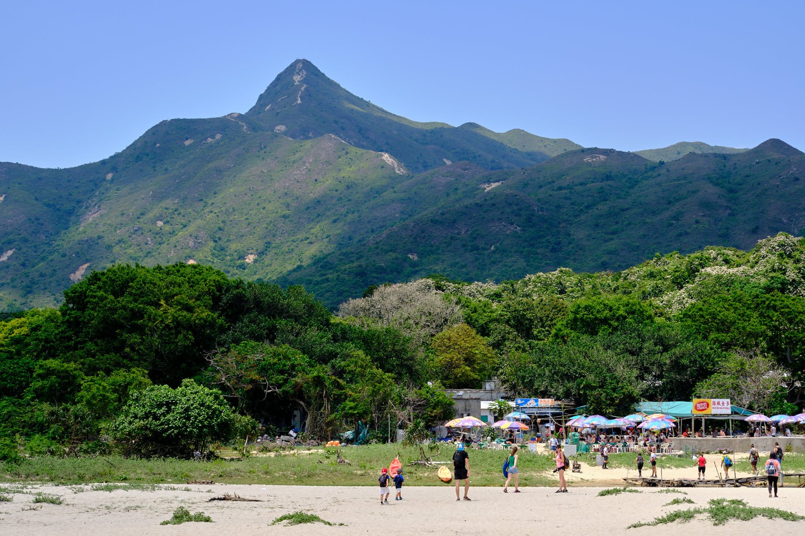 鹹田灣沙灘後方的草地、遠處的尖峭山峰以及士多店
